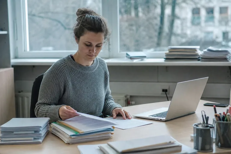 Mitarbeiterin ordnet Teilnehmerakten und Kursunterlagen an einem Schreibtisch