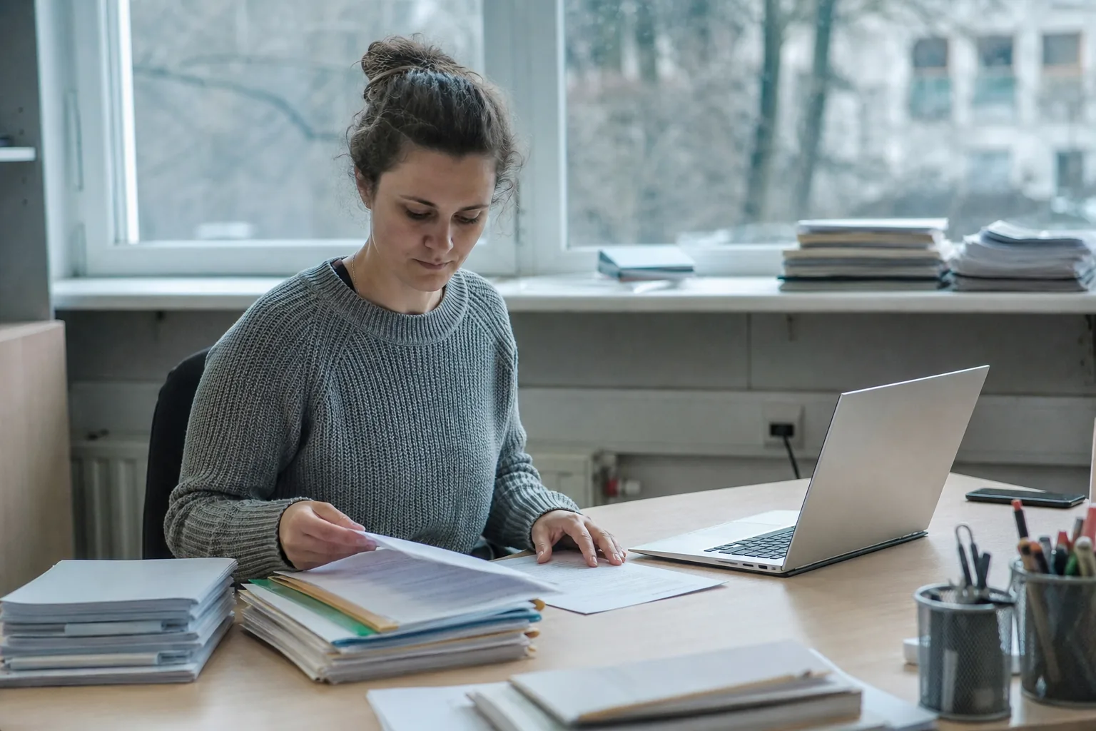 Mitarbeiterin ordnet Teilnehmerakten und Kursunterlagen an einem Schreibtisch